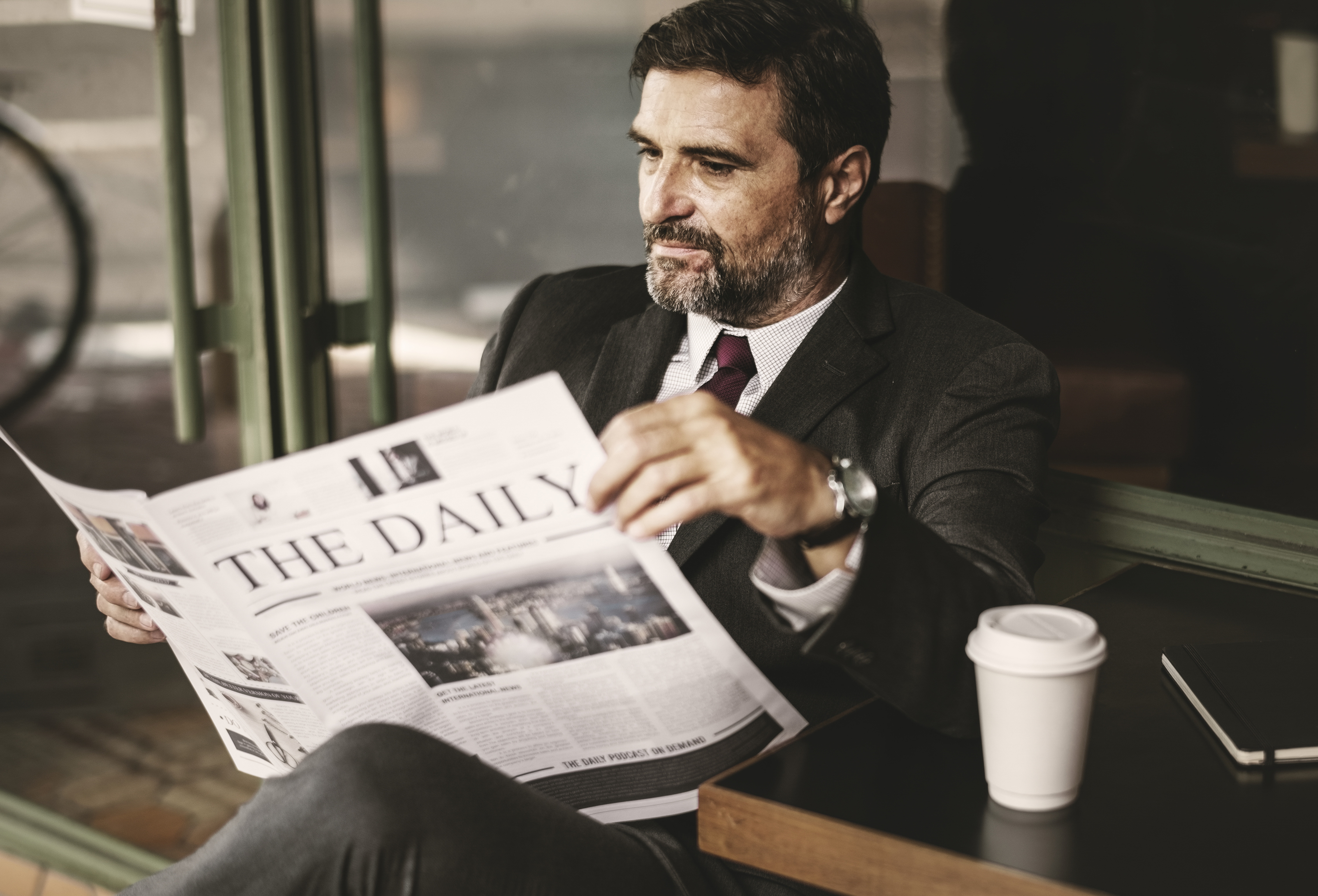 older man with salt and pepper beard reading newspaper